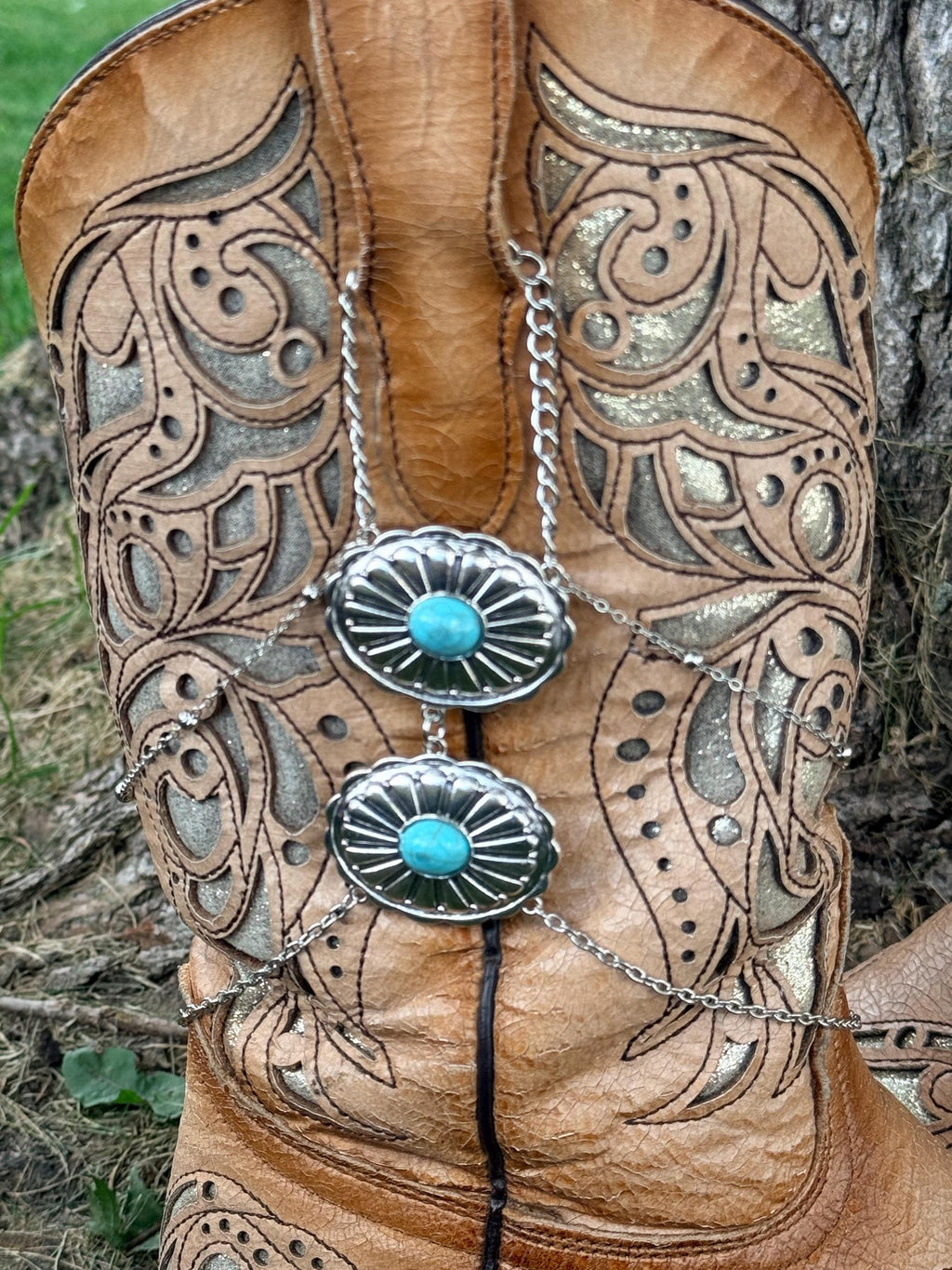 Close-up of tan tooled laser-cut cowboy boot shaft with silver multi-chain boot bracelet featuring two stacked silver oval turquoise stone concho charms, Western boot jewelry
