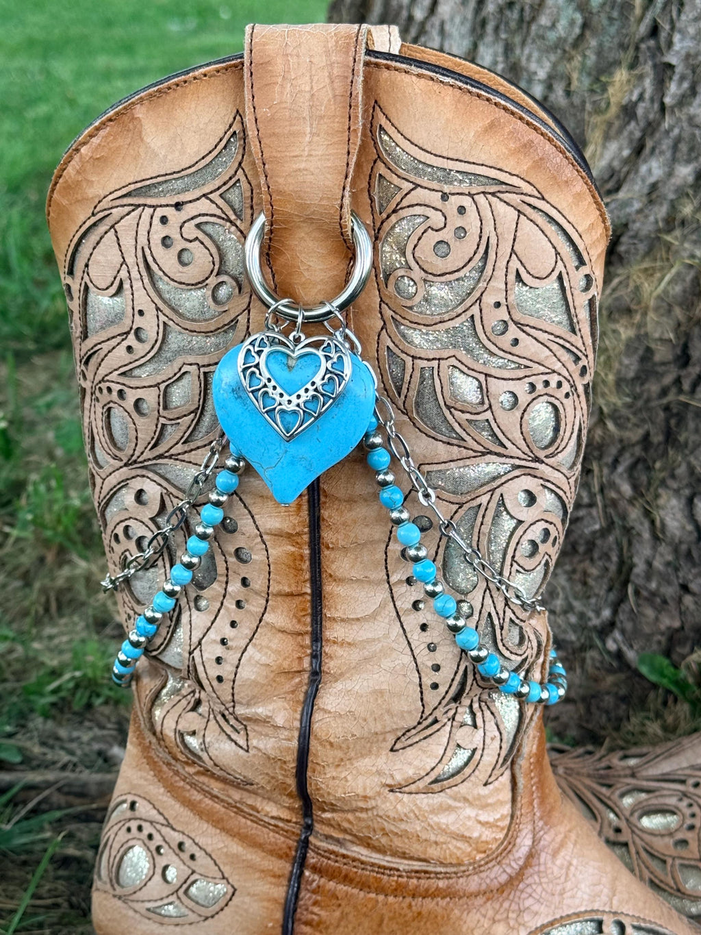 Close-up of tan tooled laser-cut cowboy boot shaft with lei boot bracelet featuring large turquoise stone heart with silver filigree overlay pendant and two-strand turquoise bead and silver chain drape