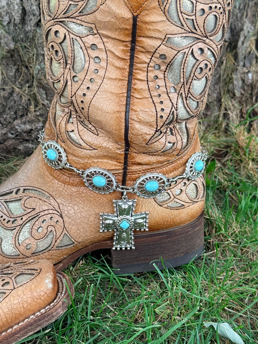 Front view of tan tooled laser-cut cowboy boot with large oval turquoise concho chain boot bracelet and large silver engraved cross pendant with turquoise center stone drop, Western boho boot accessory