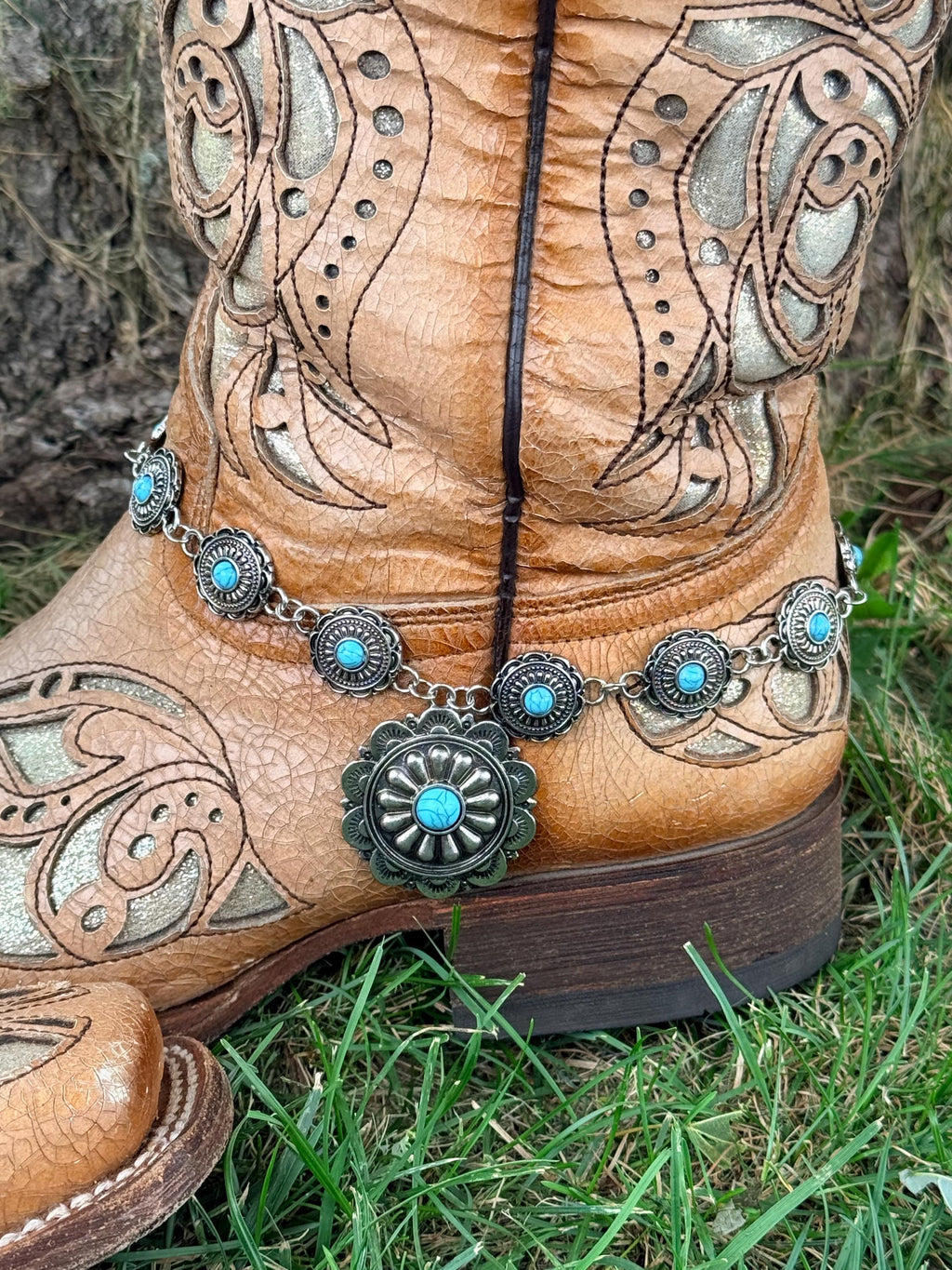 Front view of tan tooled laser-cut cowboy boot with silver linked concho chain boot bracelet and large sunburst-style turquoise center concho drop pendant, Western boho boot accessory