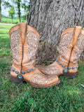 Front view of pair of tan tooled laser-cut cowboy boots against tree on grass wearing silver linked concho chain boot bracelets with large sunburst-style turquoise center drop pendant, Western boho boot jewelry set of 2