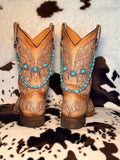 A pair of tan leather western cowboy boots with intricate tooling on cowhide rug wearing turquoise bead and silver spacer bead boot bracelet chains with large silver filigree flower concho centerpiece with three turquoise cabochon stones, Western boho boot jewelry set of 2