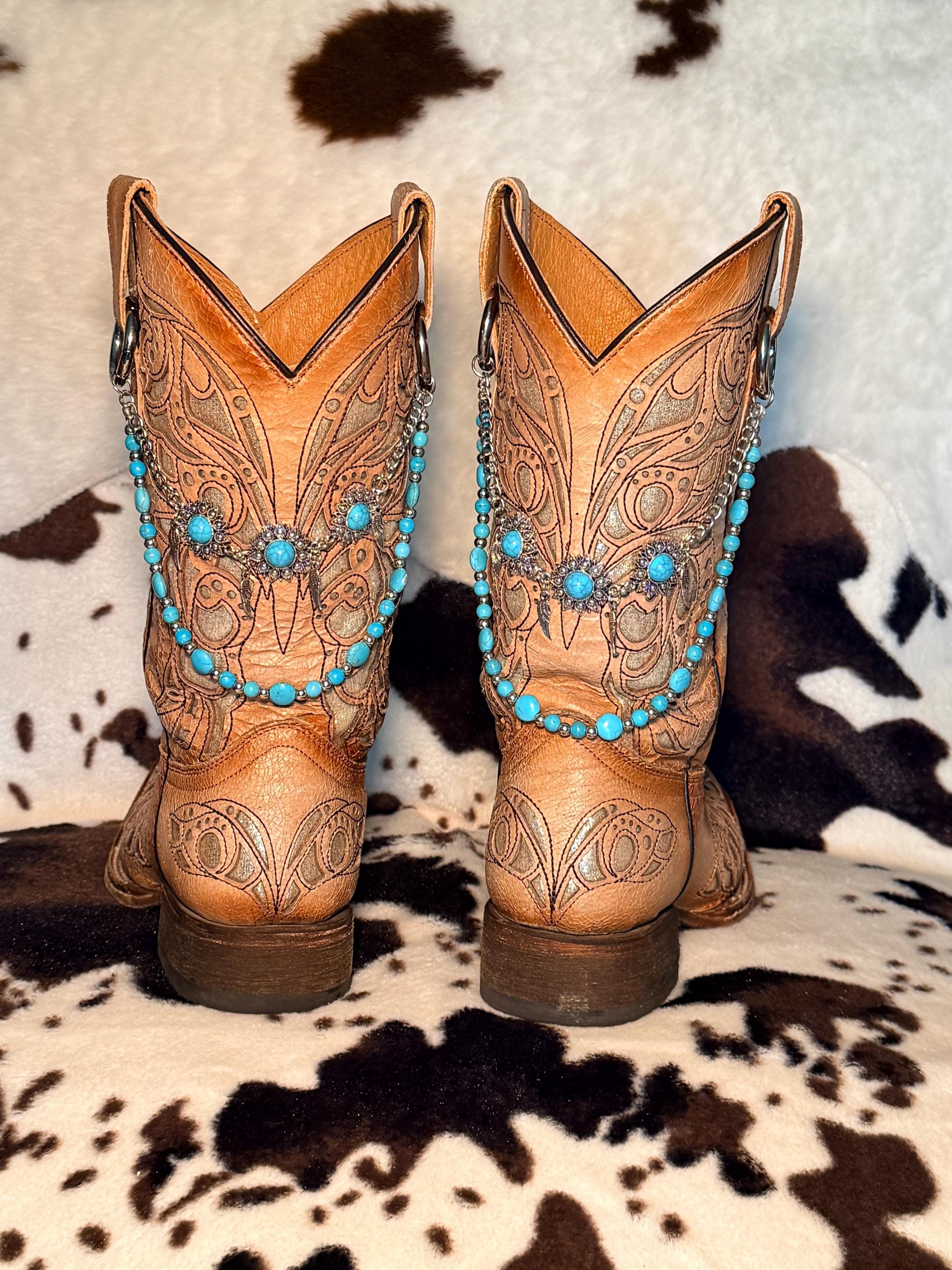 A pair of tan leather western cowboy boots with intricate tooling on cowhide rug wearing turquoise bead and silver spacer bead boot bracelet chains with large silver filigree flower concho centerpiece with three turquoise cabochon stones, Western boho boot jewelry set of 2