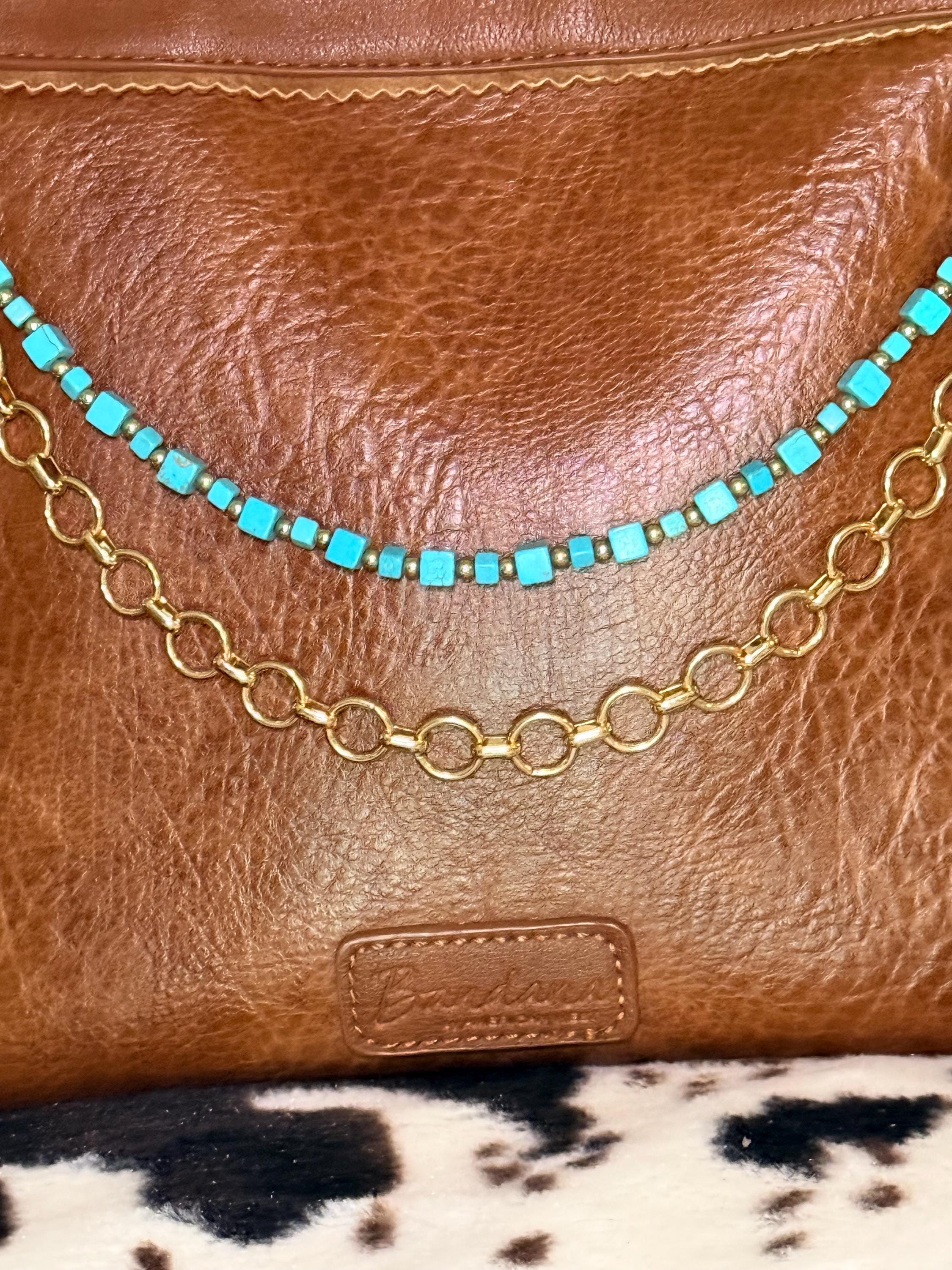 Close-up of brown distressed Bandana leather crossbody bag showing two-strand Western boho purse chain with turquoise square cube bead strand with small gold rondelle spacers between each bead above and bold gold round link chain below, layered Western boho handbag accessory detail