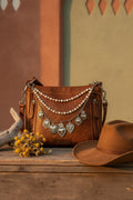Front view of brown distressed Bandana leather crossbody bag with four-strand Western boho purse chain featuring small and larger faux pearl bead strands, delicate silver cable chain, and silver curb chain with seven large ornate silver sacred heart charms including large flaming sacred heart with sunburst rays at center, flaming sacred heart with wings, and filigree-bordered sacred heart with flower detail