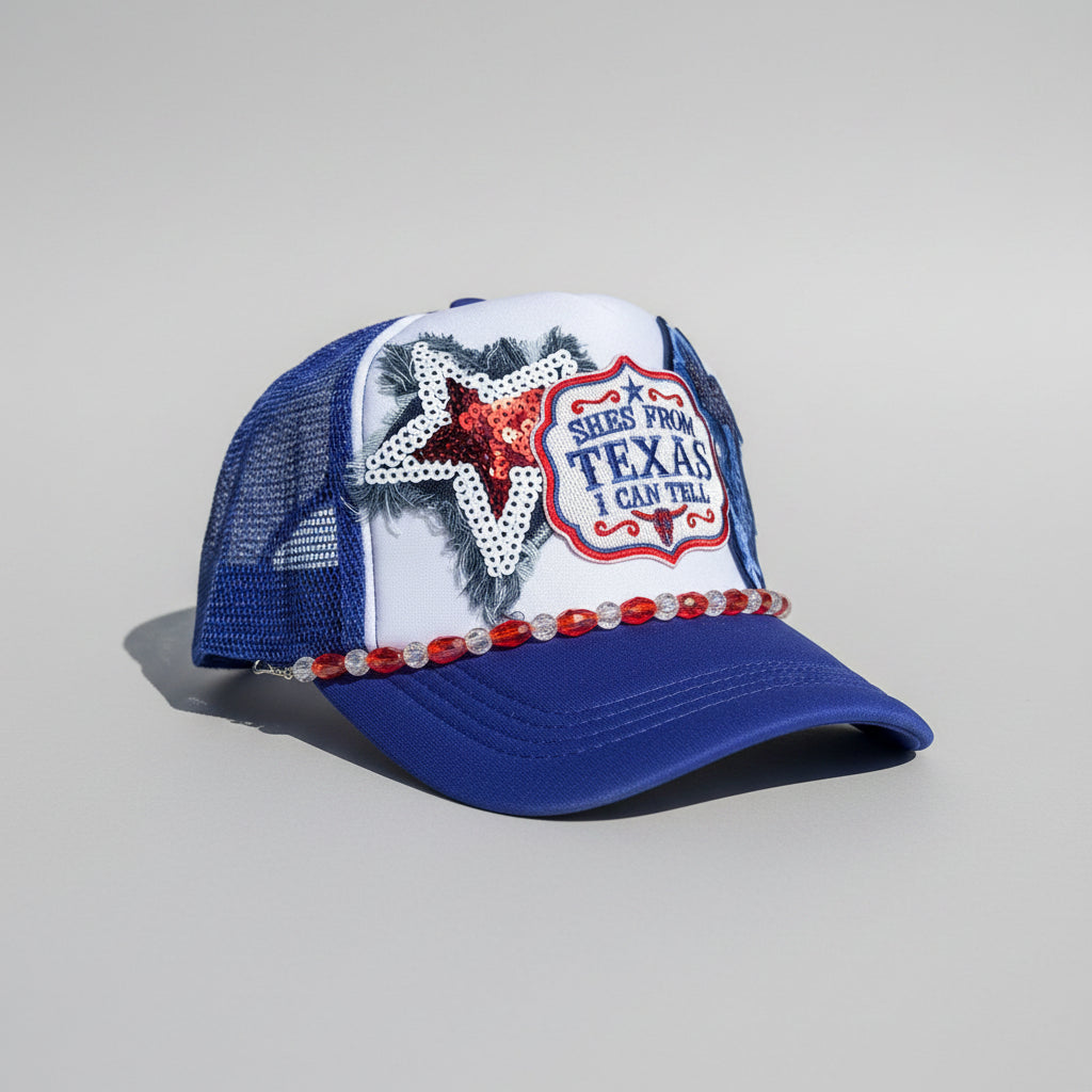 A blue and white trucker hat with a glittery red star, a 'Texas' patch, and red rhinestone trim,