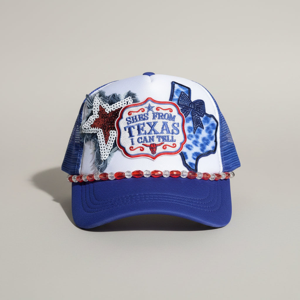 A blue and white trucker hat with a 'Texas' patch, a rhinestone star, and a blue Texas state outline on the front panels, 
