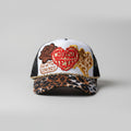 A trucker hat with a white front panel featuring embroidered designs including a rose, a red heart reading 'CHOOSIN TEXAS,' and a Texas-shaped outline, paired with a leopard-print brim and black mesh sides.